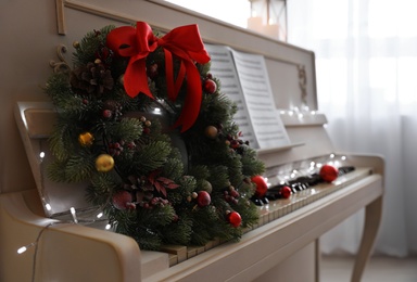 Photo of White piano with decorative wreath indoors, closeup. Christmas music