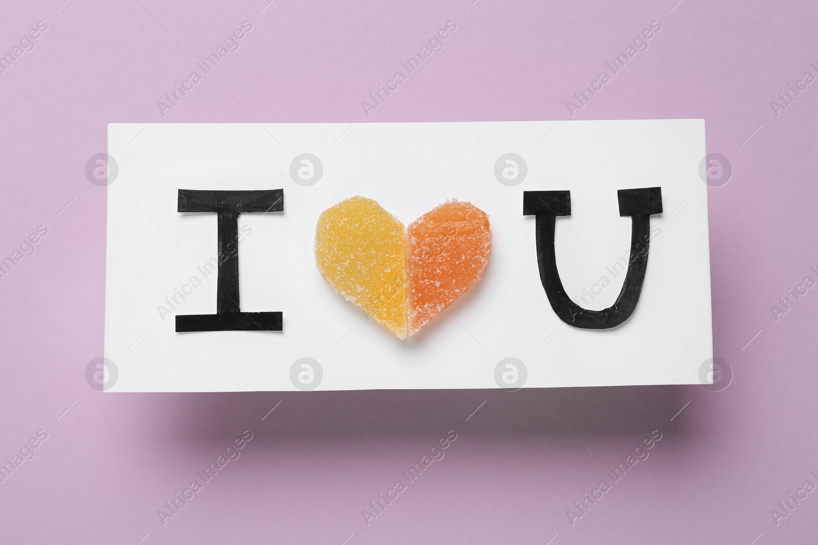 Photo of Card with phrase I Love You made of jelly candies and black letters on violet background, top view