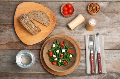 Tasty green beans with cheese and tomatoes served for dinner on wooden table, top view