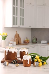 Delicious Easter cakes with sprinkles, painted eggs and beautiful tulips on white marble table in kitchen
