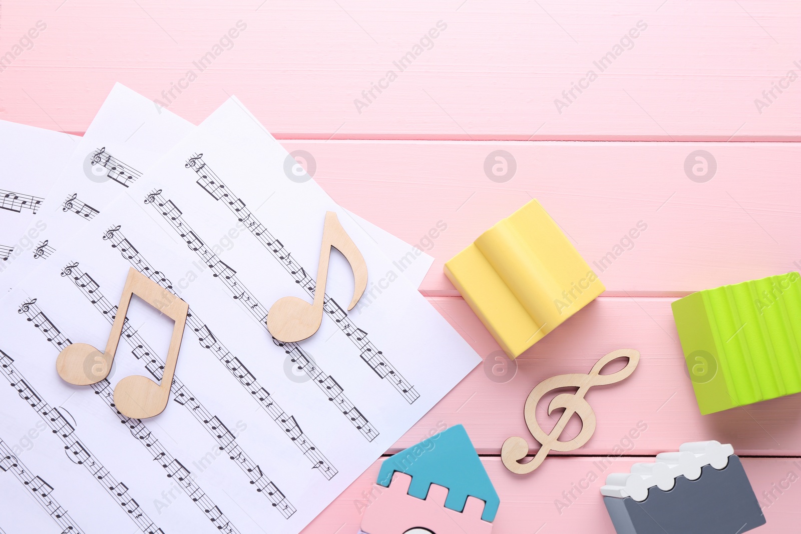 Photo of Notes, music sheets and toys on pink wooden table, top view with space for text. Baby song concept