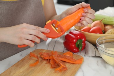 Woman peeling fresh carrot at white marble table, closeup