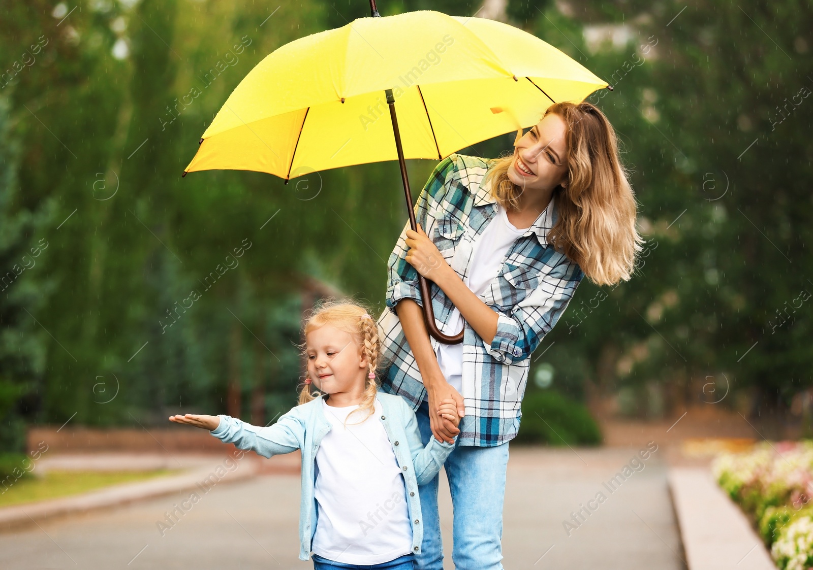 Photo of Happy mother and daughter with umbrella under rain in park