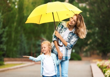 Happy mother and daughter with umbrella under rain in park