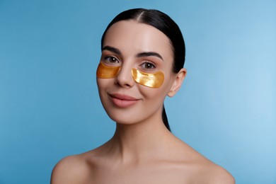 Photo of Beautiful young woman with under eye patches on light blue background