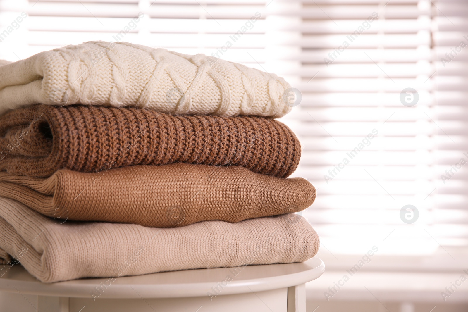 Photo of Stack of folded warm sweaters on white table indoors, closeup