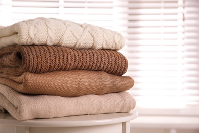 Stack of folded warm sweaters on white table indoors, closeup