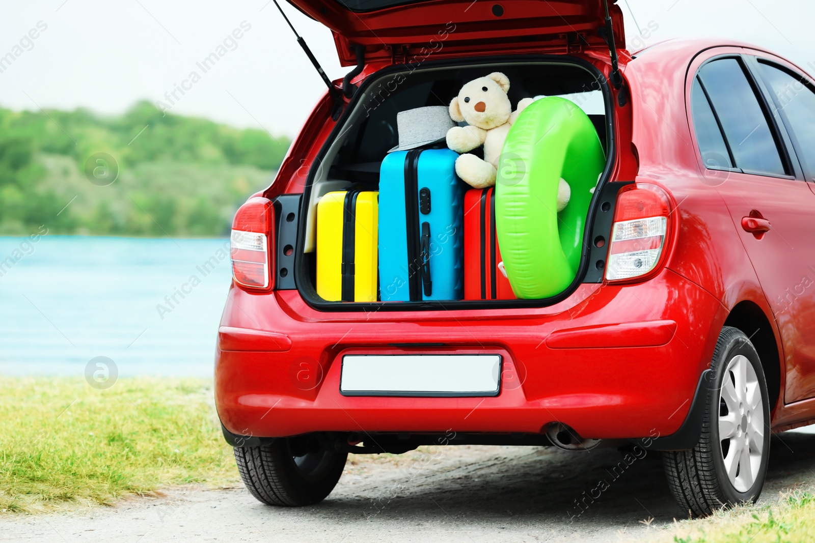 Photo of Suitcases, toys and hat in car trunk on riverside