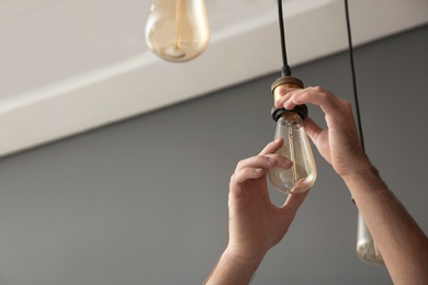 Photo of Man changing lamp light bulb indoors, closeup. Space for text