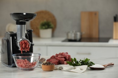 Electric meat grinder with beef mince, parsley, salt and peppercorns on white table in kitchen