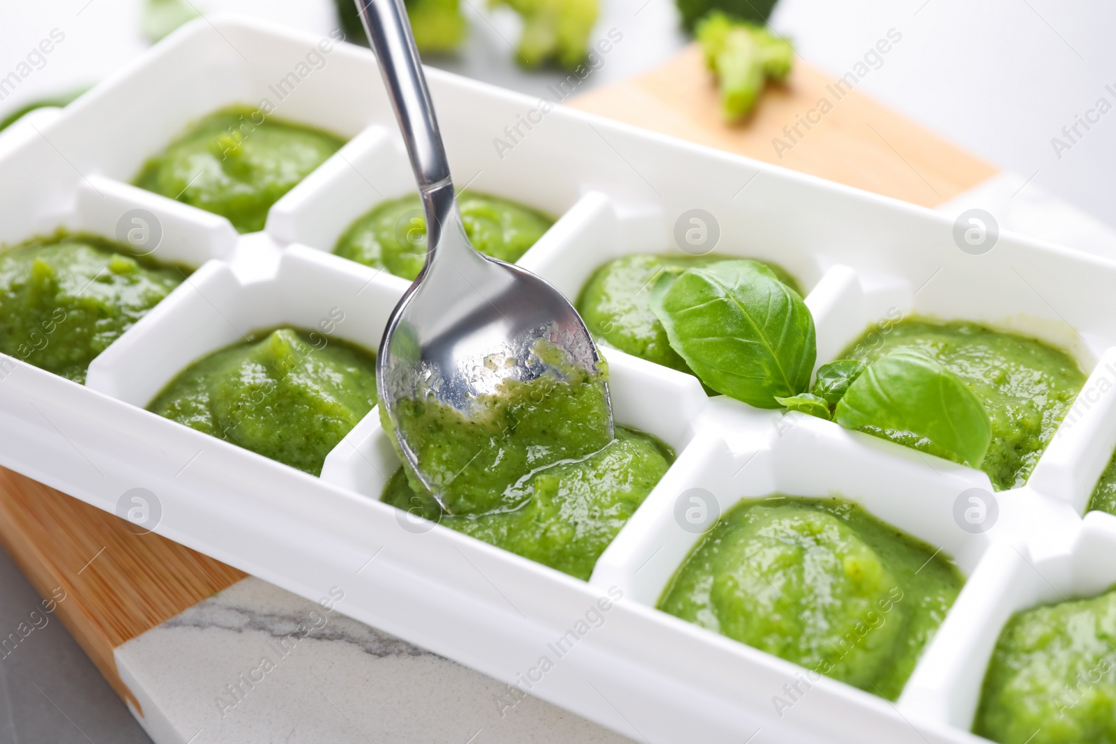 Photo of Putting puree with spoon into ice cube tray on table, closeup. Ready for freezing