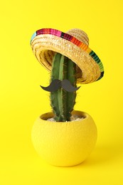 Photo of Cactus with Mexican sombrero hat and fake mustache on yellow background