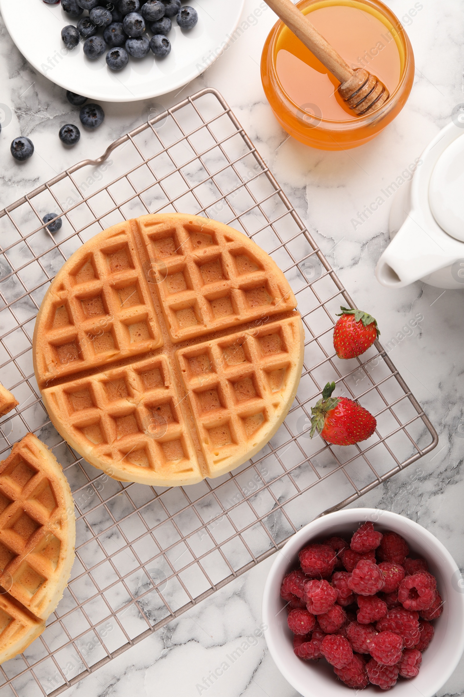 Photo of Tasty Belgian waffles with fresh berries and honey on white marble table, flat lay