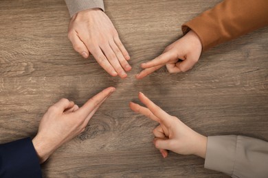 Closeup of people playing rock, paper and scissors on wooden background, top view