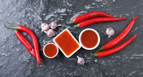 Photo of Spicy chili sauce, peppers and garlic on black textured table, flat lay