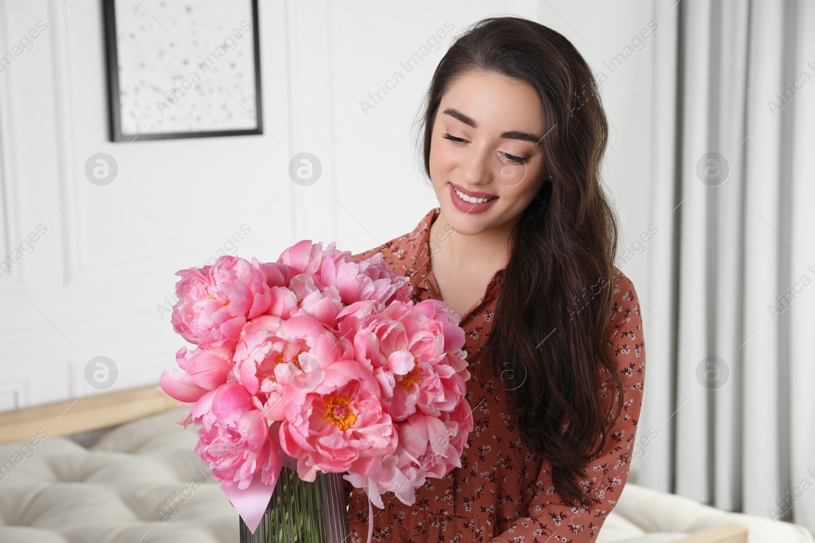 Photo of Beautiful young woman with bouquet of pink peonies at home