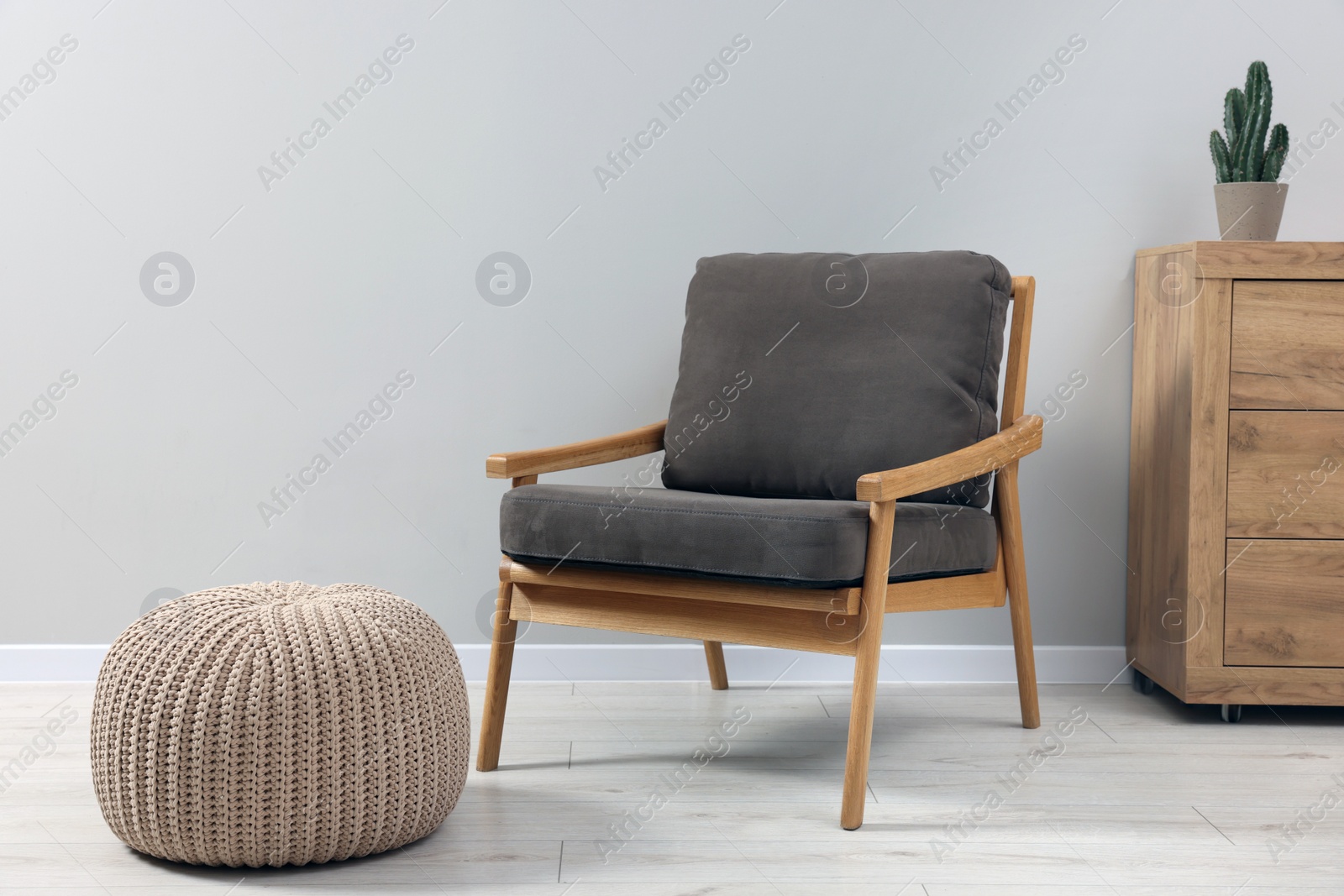 Photo of Comfortable armchair, chest of drawers and pouf near light grey wall indoors. Interior design