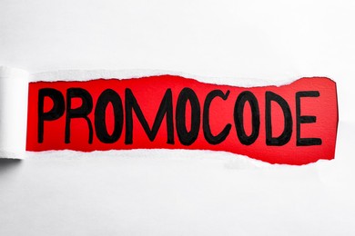 Photo of Word Promocode written on red background, view through hole in white paper