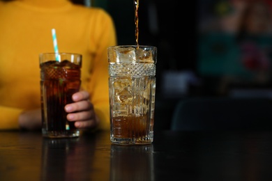 Photo of Pouring refreshing cola into glass and blurred woman on background