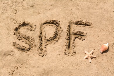 Abbreviation SPF written on sand, seashell and starfish at beach, top view