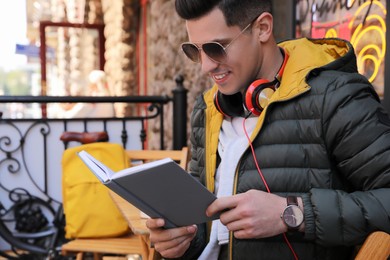 Photo of Handsome man reading book in outdoor cafe