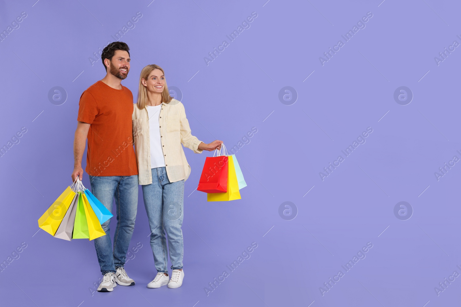 Photo of Family shopping. Happy couple with many colorful bags on violet background. Space for text