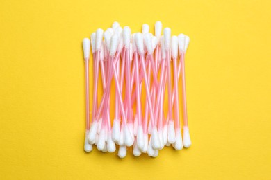 Photo of Heap of cotton buds on yellow background, top view
