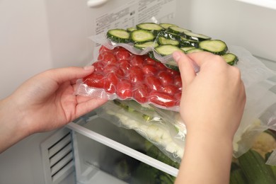 Photo of Woman putting vacuum bags with vegetables into fridge, closeup. Food storage