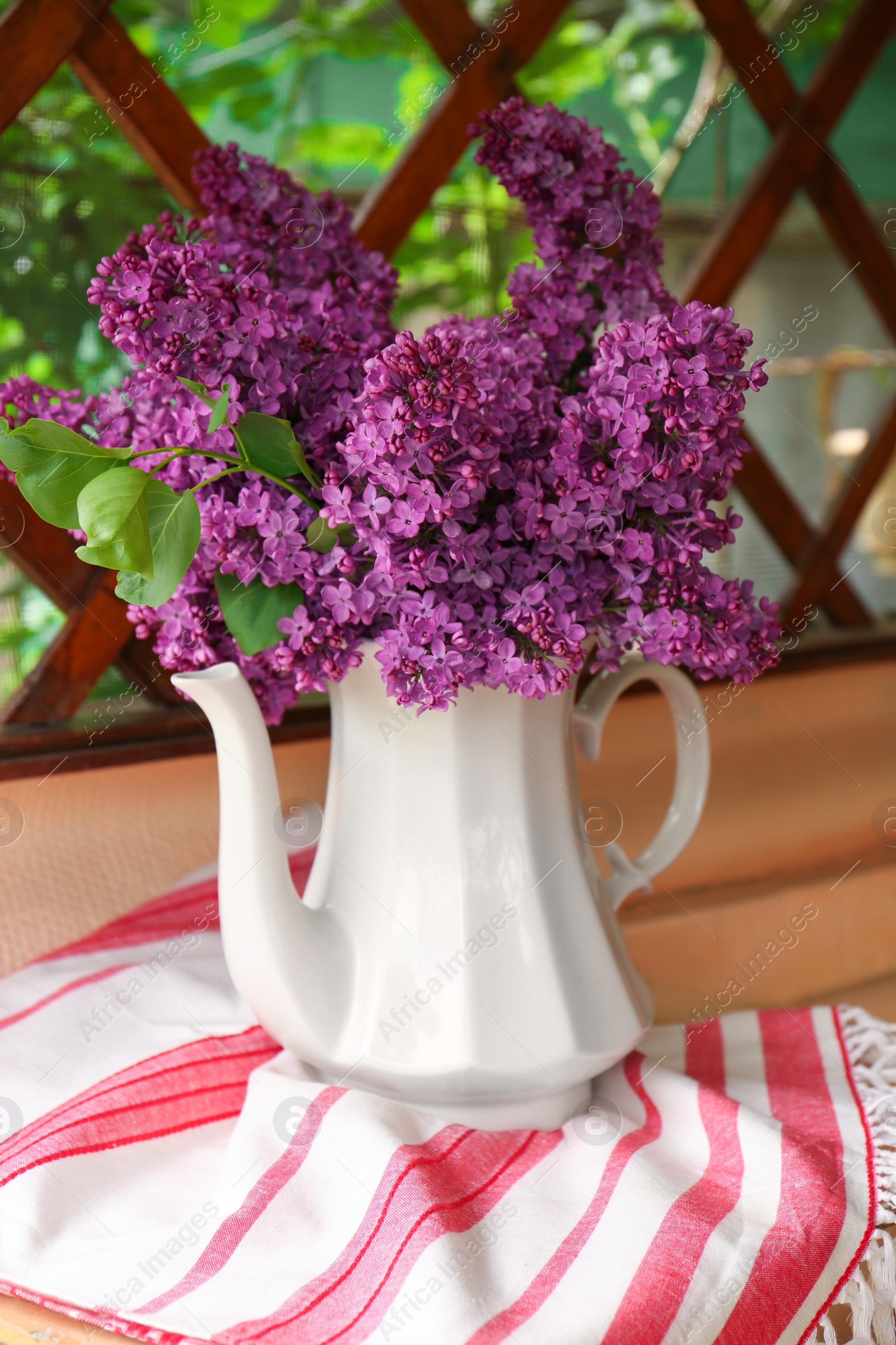 Photo of Beautiful lilac flowers in teapot near window indoors