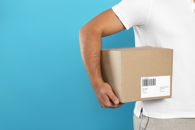 Photo of Courier holding cardboard box on light blue background, closeup. Space for text