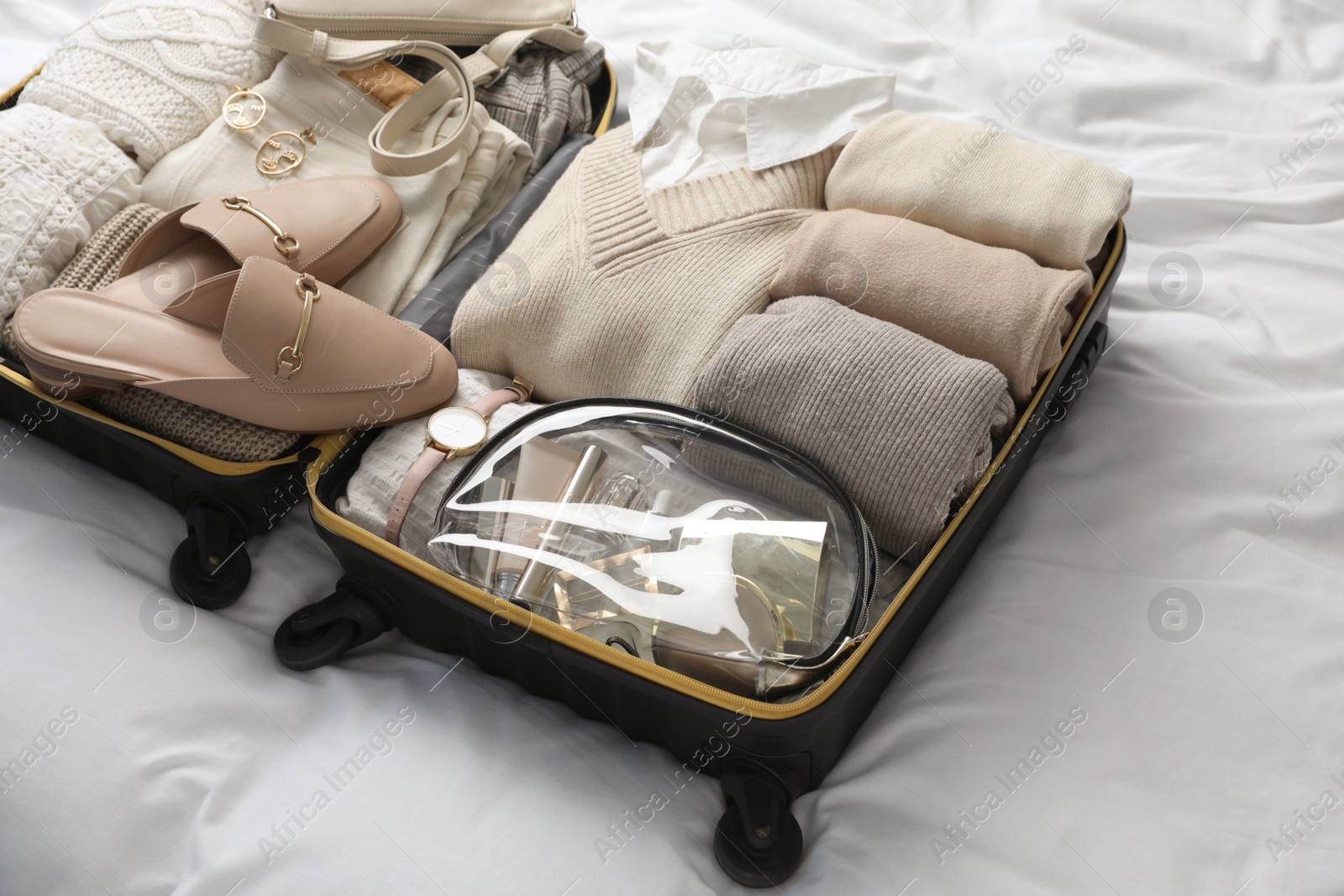 Photo of Open suitcase with folded clothes, shoes and accessories on bed