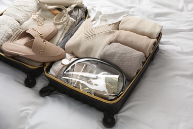 Open suitcase with folded clothes, shoes and accessories on bed