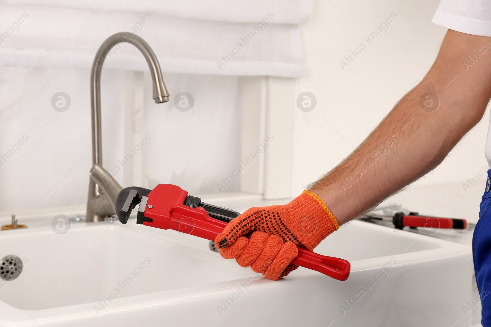 Photo of Man with pipe wrench near sink in kitchen, closeup. Water tap installation