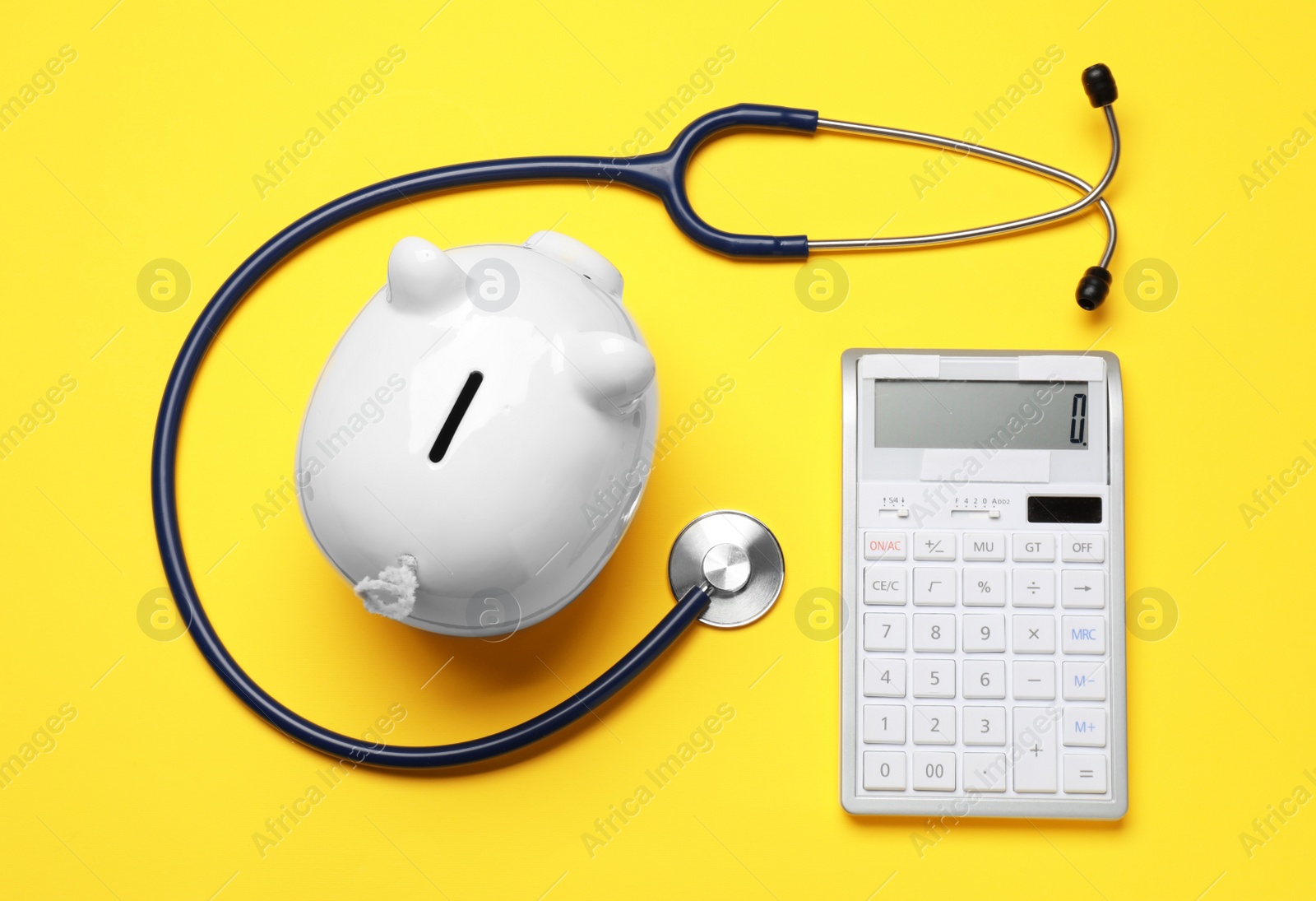 Photo of Piggy bank, calculator and stethoscope on yellow background, flat lay. Medical insurance
