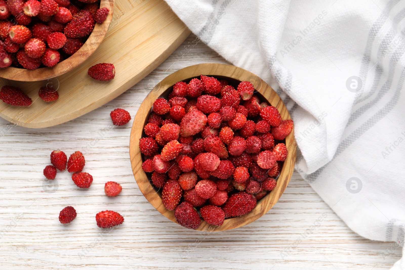 Photo of Fresh wild strawberries in bowls on white wooden table, flat lay