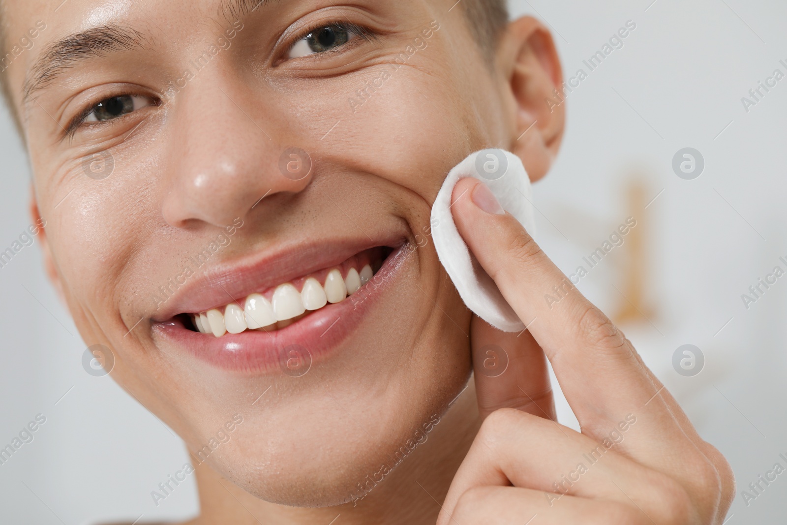 Photo of Handsome man cleaning face with cotton pad against blurred background, closeup