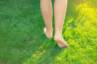 Teenage girl walking barefoot on green grass outdoors, closeup. Space for text