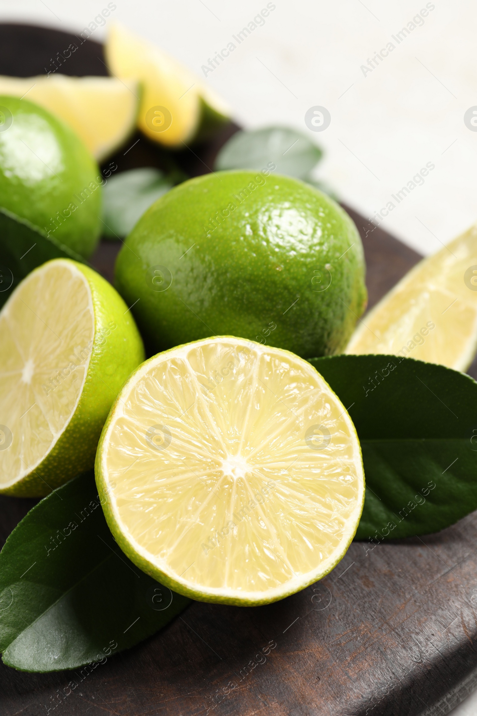 Photo of Fresh ripe limes and green leaves on black board, closeup