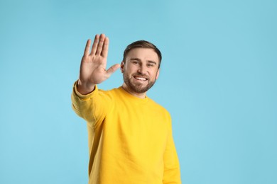 Photo of Happy young man waving to say hello on light blue background