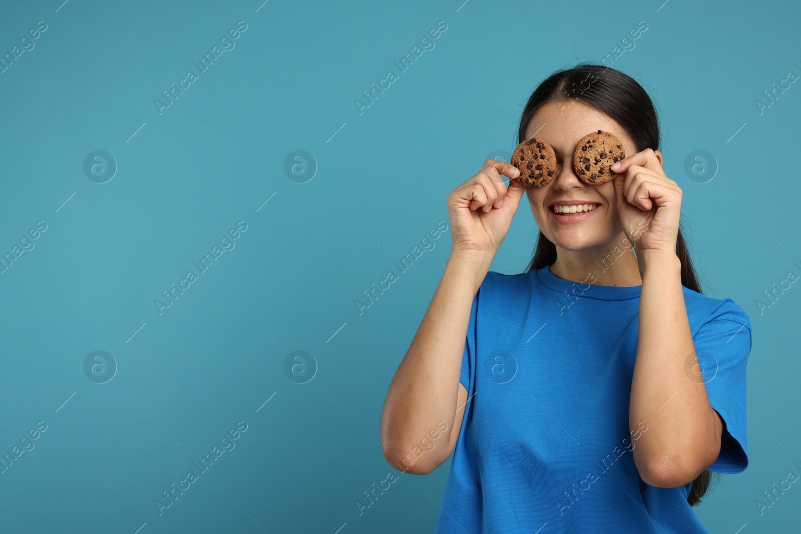 Photo of Young woman with chocolate chip cookies on light blue background, space for text