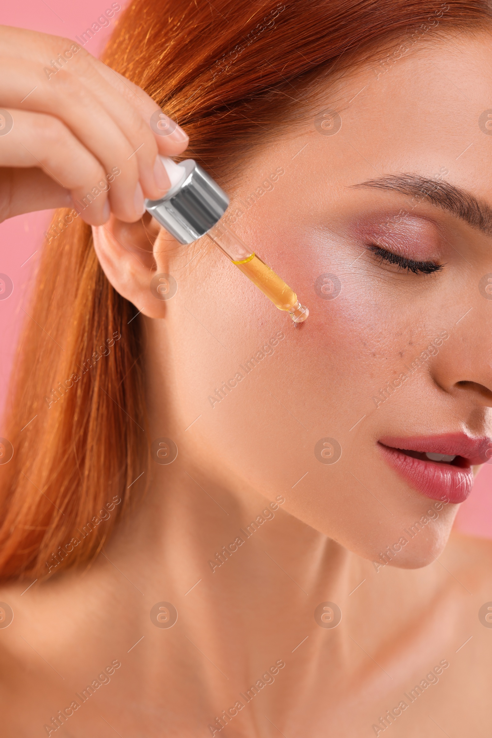 Photo of Beautiful young woman applying cosmetic serum onto her face on pink background, closeup