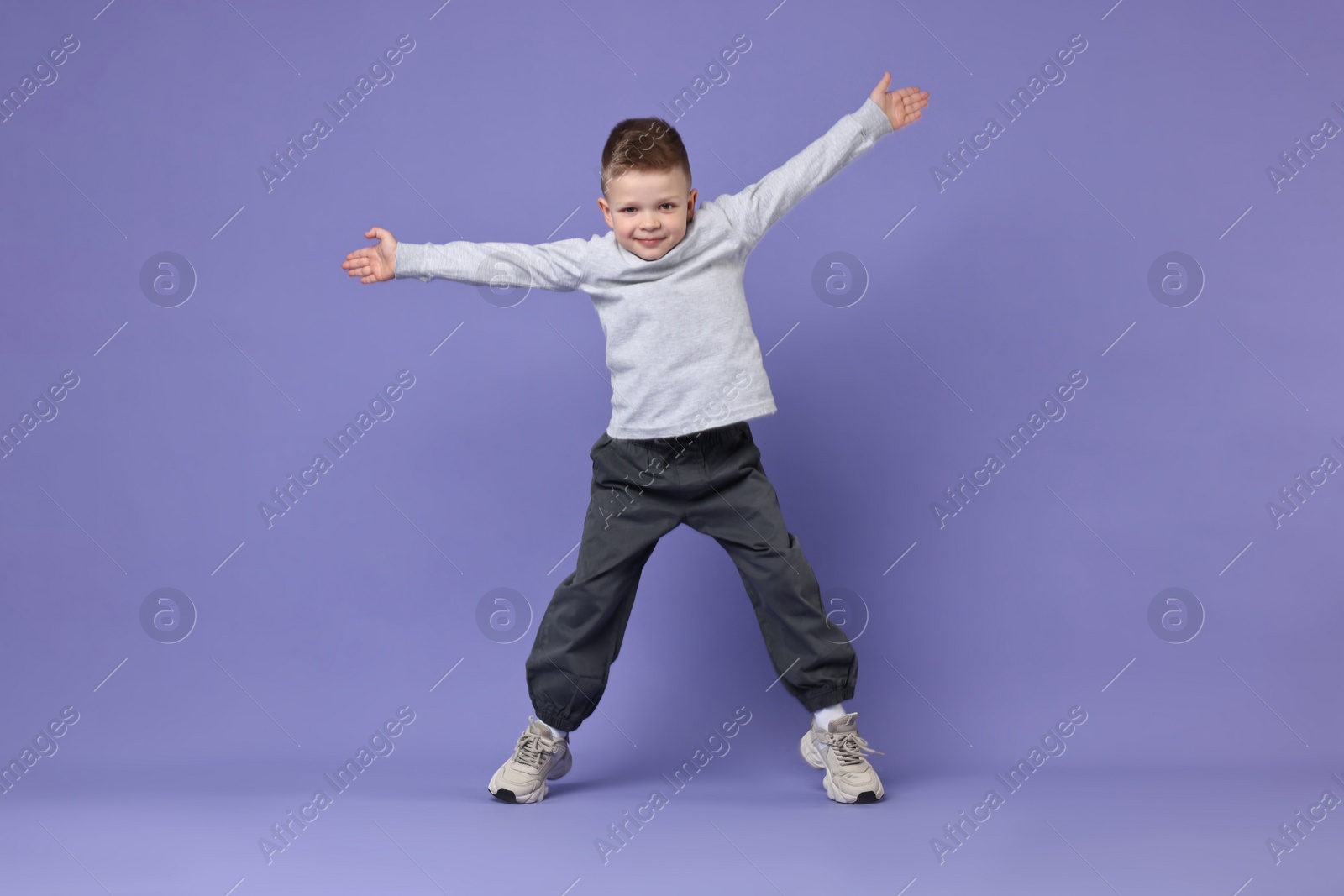 Photo of Happy little boy dancing on violet background