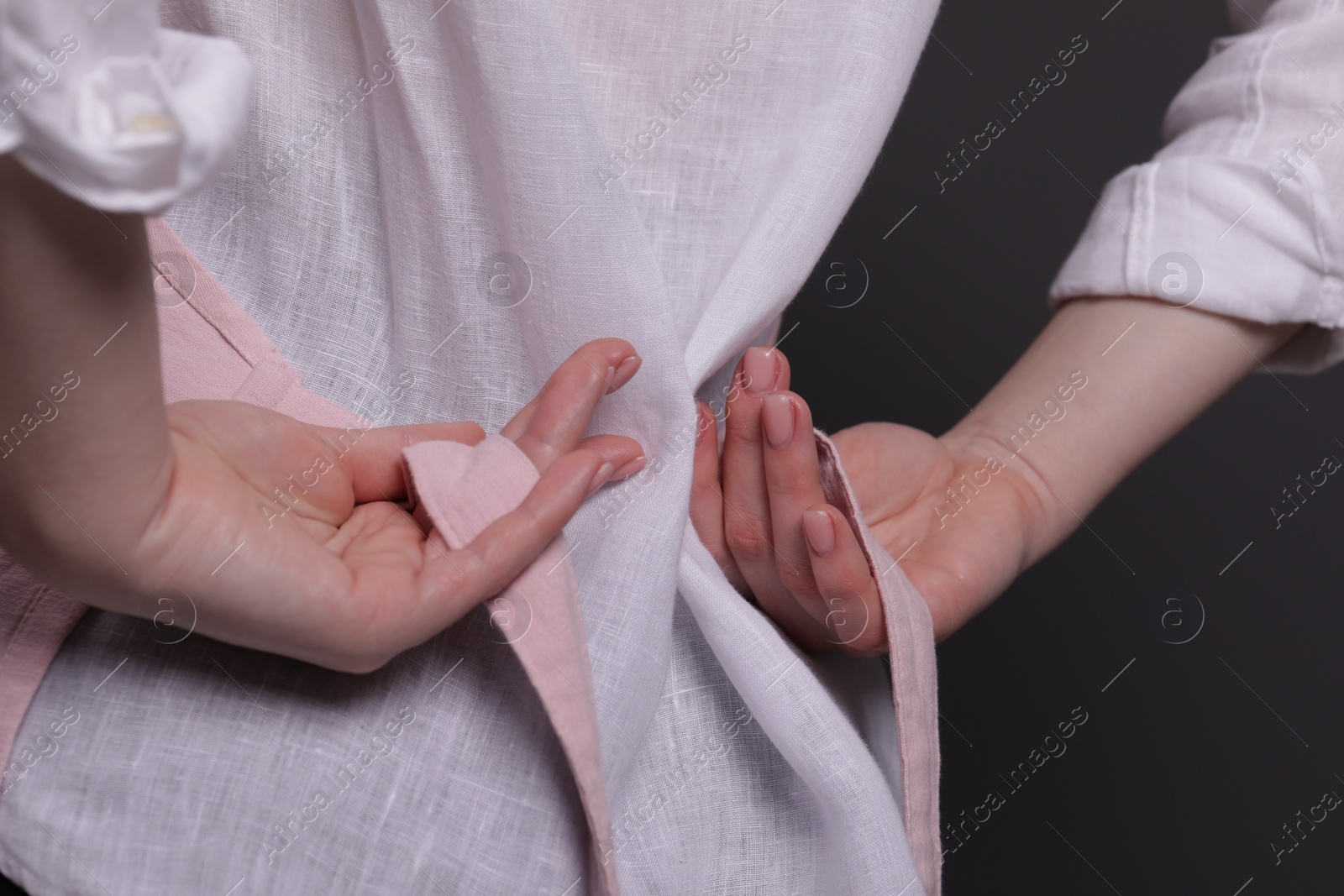 Photo of Woman putting on pink apron against grey background, closeup