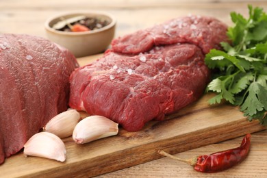 Pieces of raw beef meat, parsley, garlic and spices on wooden table, closeup