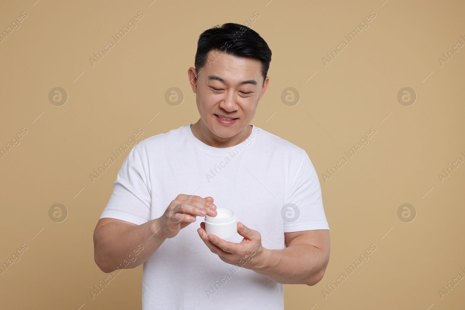 Photo of Handsome man with jar of body cream on light brown background