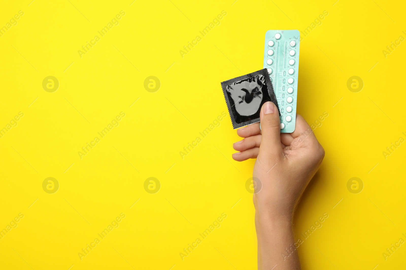 Photo of Woman holding condom and birth control pills on yellow background, top view with space for text. Safe sex