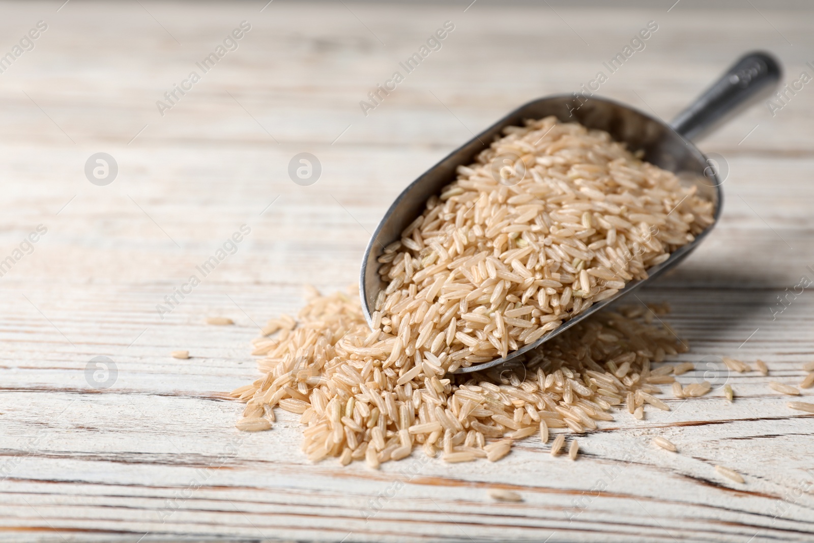 Photo of Uncooked brown rice in metal scoop on wooden table