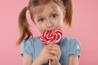 Photo of Portrait of cute girl licking lollipop on pink background