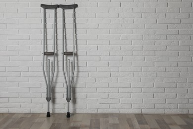 Photo of Pair of axillary crutches near white brick wall. Space for text
