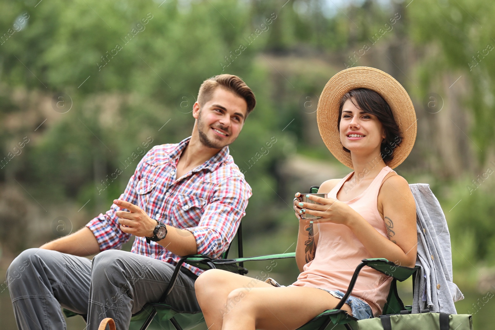 Photo of Young couple resting near forest, outdoors. Camping season